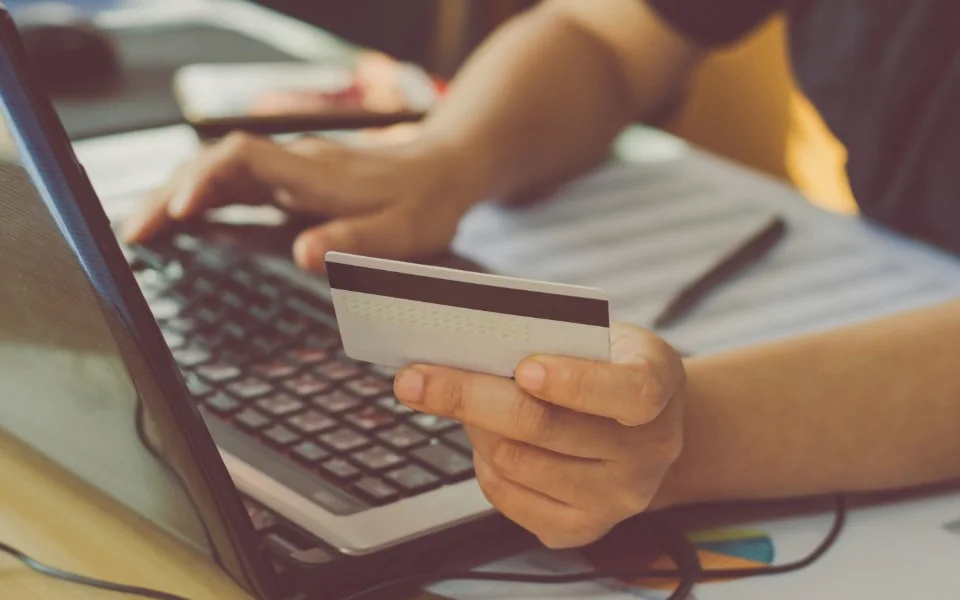 Hands at a laptop keyboard holding a bank card
