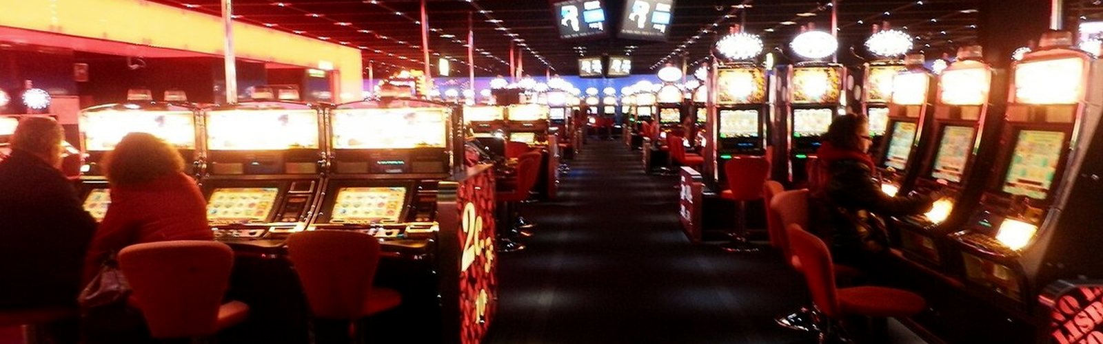 A casino floor lined with slot machines under red light